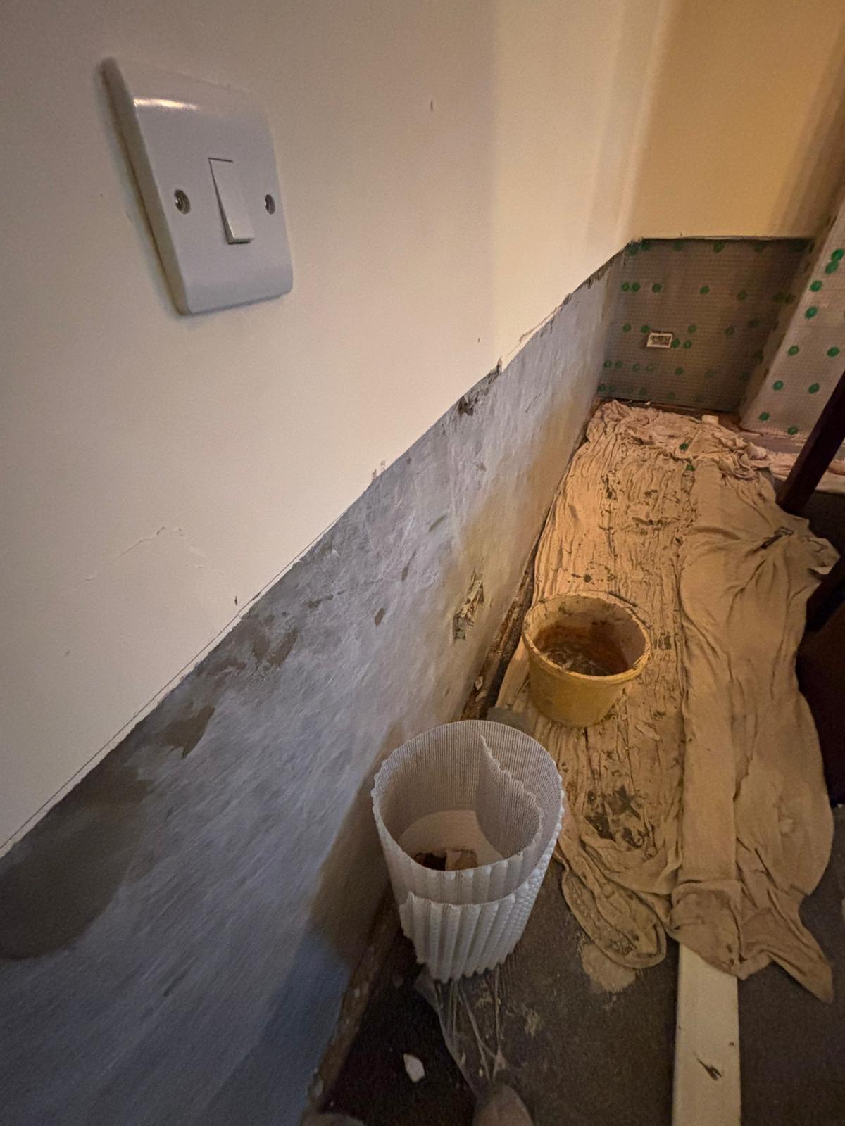 Wall stripped of damp plaster at low level, with dust sheets down